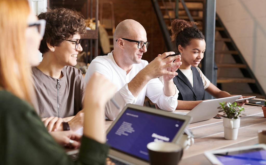 A diverse group of professionals sitting at a table with laptops, collaborating on a project